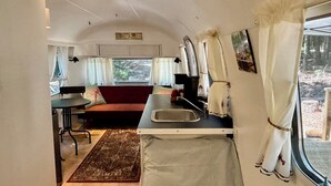 Interior compacto de una caravana con kitchenette, comedor y zona de estar con sofá.