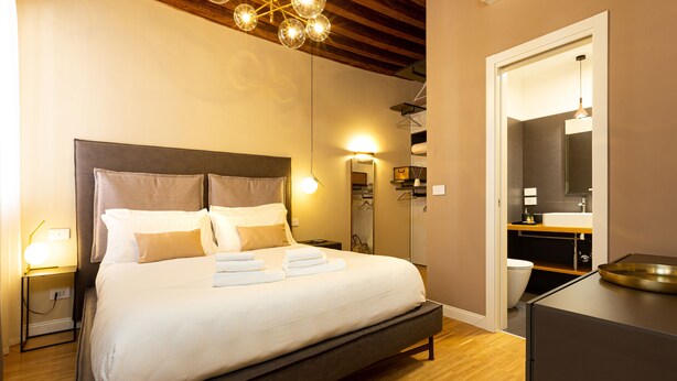 A neatly made bed with white linens and a wooden headboard, a bedside lamp, and a modern chandelier. - Two bedroom apartment with ensuite bathrooms in a perfect location. (Venezia)
