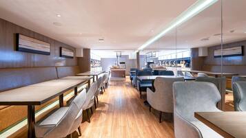 A modern restaurant interior with wooden flooring, long communal tables, and cushioned seating.