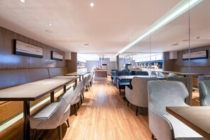 Un interior de restaurante moderno con suelo de madera, mesas comunitarias largas y asientos acolchados.