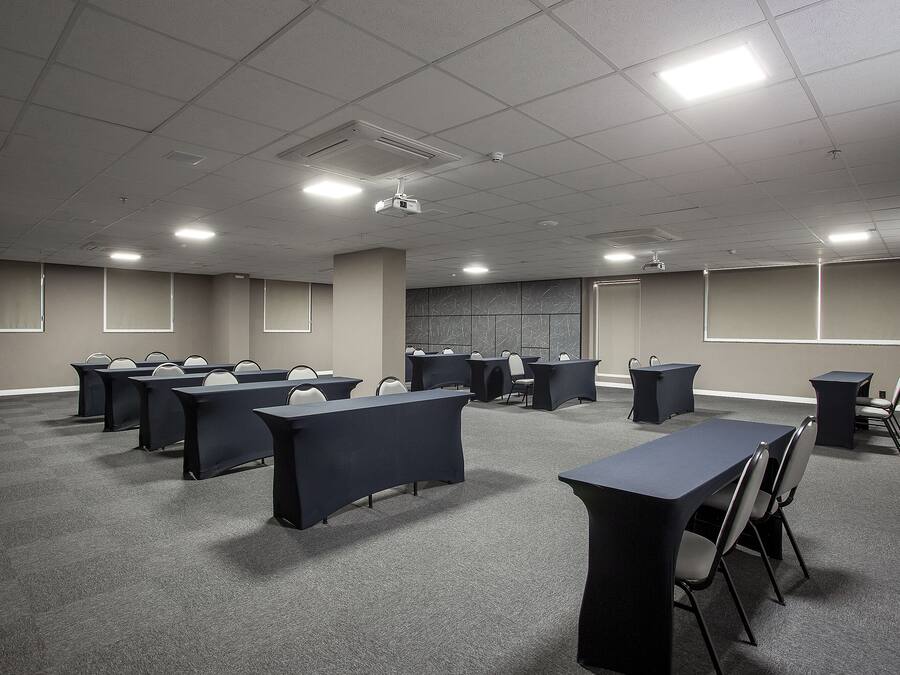 Un salón de conferencias con varias mesas y sillas, un proyector y una pantalla grande.