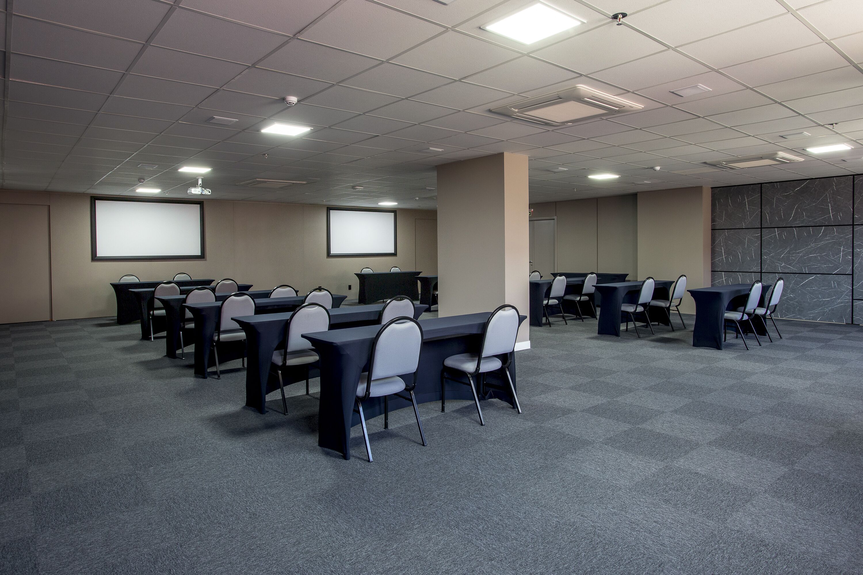 A conference room with multiple tables and chairs, a projector screen, and a marble-patterned wall.