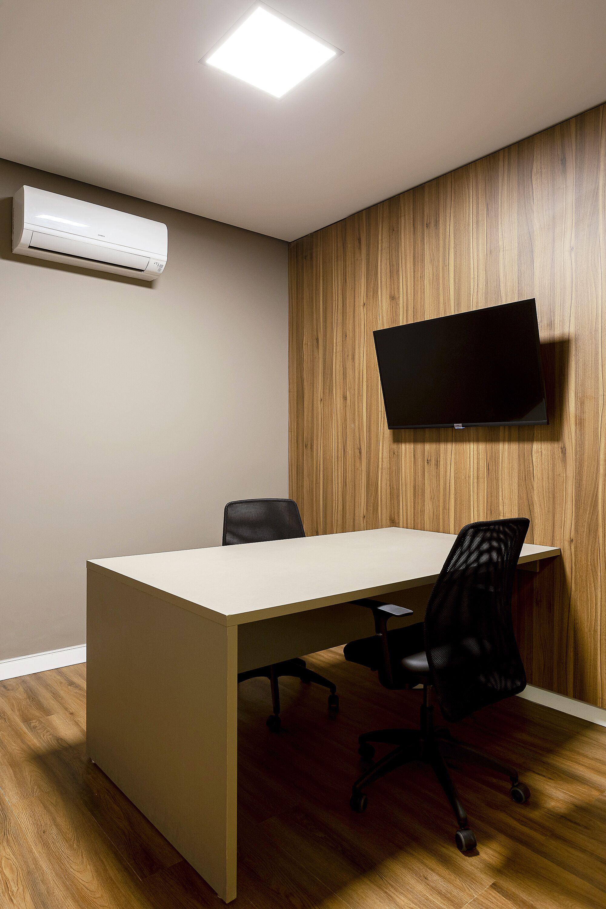 Uma sala de conferências com uma mesa comprida, duas cadeiras, uma TV de tela plana na parede e um aparelho de ar condicionado.