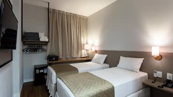 A hotel room with two beds, a bedside table with a lamp, a wardrobe, and a mirror.