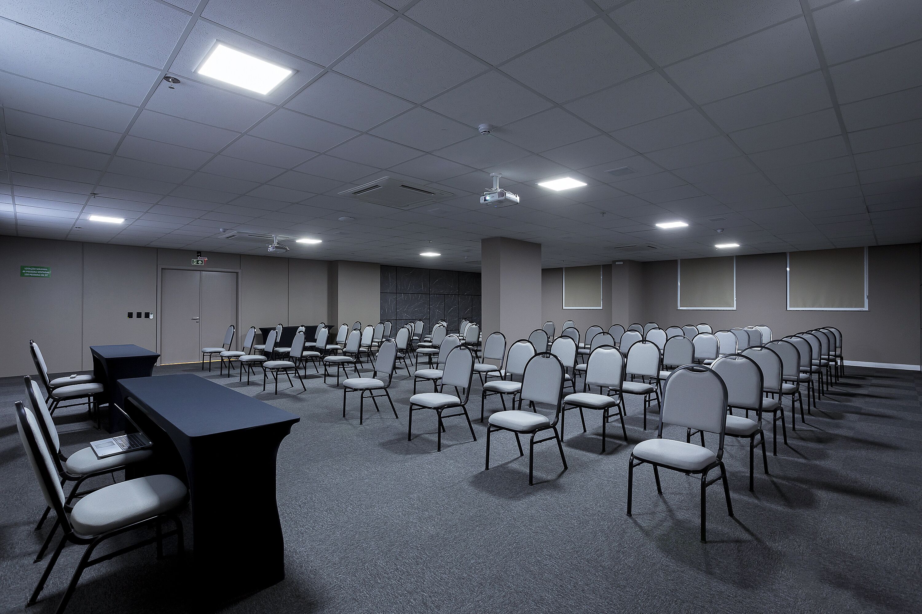 A conference room with rows of chairs, a long table, and ceiling lights.