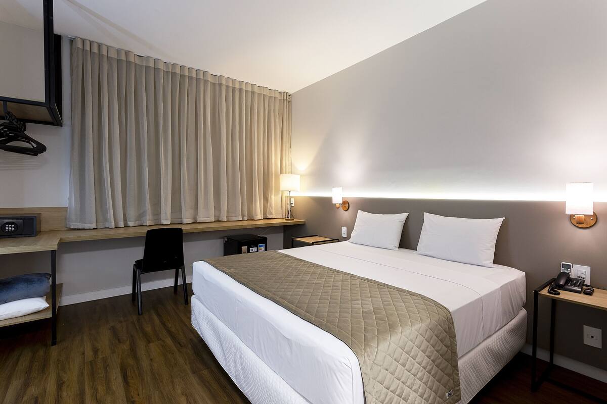 A hotel room with a bed, bedside tables, a desk, a chair, and a TV.