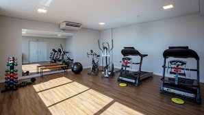 A gym with exercise equipment, a bench, and a mirror reflecting the room. - Nacional Inn Rondonopolis (Rondonópolis)