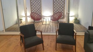 Ett rum med två mörka stolar, ett litet bord och ett trägolv. Det finns två gallerliknande skärmar med lampor bakom.
