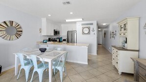 Una cocina moderna con armarios blancos, una isla central y un comedor con sillas azul claro.