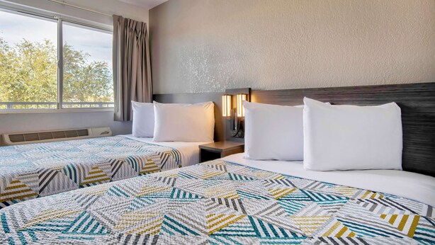 A hotel room with two beds, a large window, and a view of trees. - Studio 6 Albuquerque, NM – Midtown (Albuquerque)