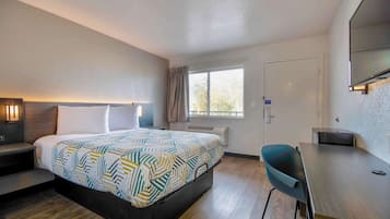 Une chambre d’hôtel avec un lit, une table de chevet, un bureau, une chaise et une grande fenêtre.