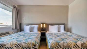 Quarto de hotel com duas camas, janela com cortinas, luminária fixada na parede e uma pequena mesa de cabeceira.