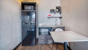 A compact kitchenette with a refrigerator, microwave, coffee maker, and a small table. - Studio 6 Albuquerque, NM – Midtown (Albuquerque)