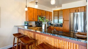 A modern kitchen with wooden cabinets, a stainless steel refrigerator, and a marble countertop. - Private Oceanfront Penthouse Lae Nani 231, New split A/C, Parking, AMAZING VIEW! (Kapaʻa)