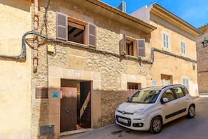 Um carro branco estacionado em frente a um edifício de pedra com várias janelas e persianas, uma porta visível e uma placa indicando o quarto número 31.