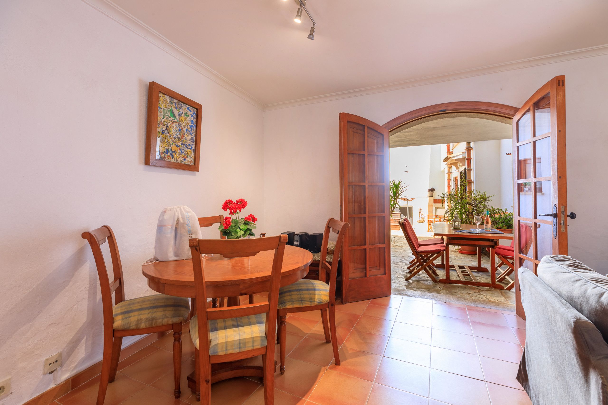 A dining area with a round wooden table, four chairs, and a vase with red flowers.