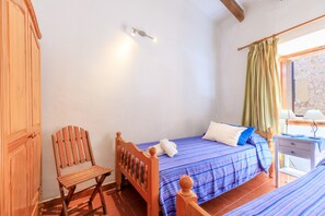 A bedroom with a bed, a wooden chair, a nightstand, and a window with curtains. - Casa Torres (Pollensa / Pollença)