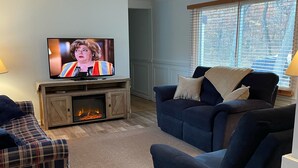 Een woonkamer met een televisie, een open haard, een blauwe bank en een gestreepte bank.