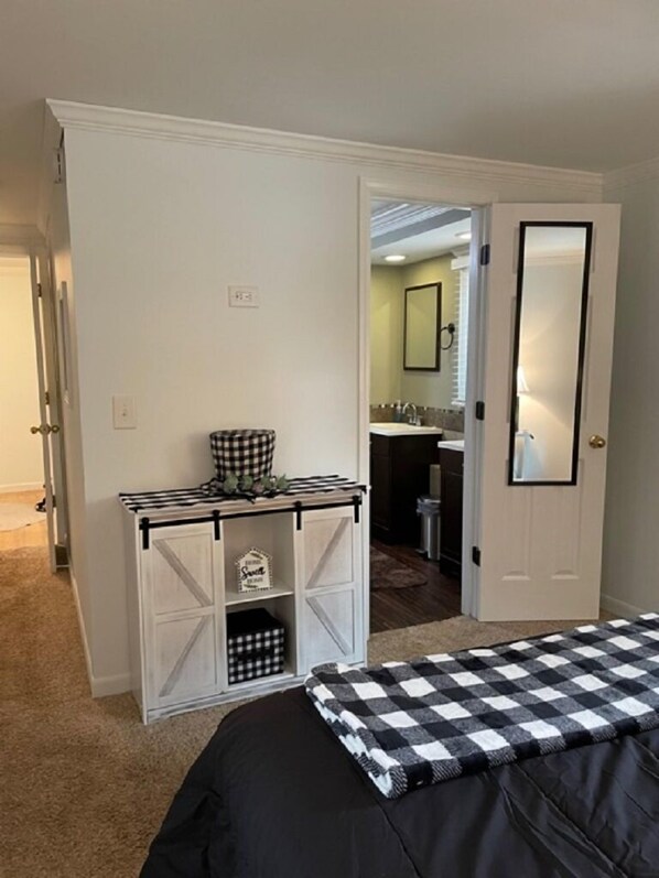 A bedroom with a bed, a dresser, a mirror, and a door leading to a bathroom.