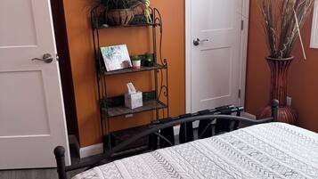 A bedroom with a bed, a shelf with plants, a door, and a wall with a framed picture.