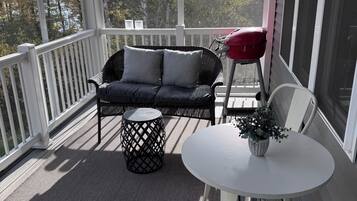 A covered porch with a sofa, a small table with a plant, and a grill.