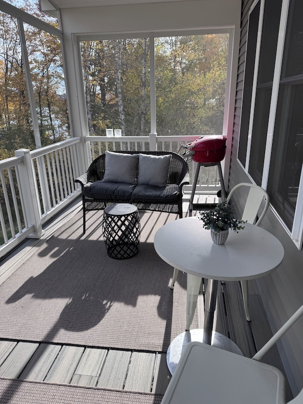 A covered porch with a sofa, a small table with a plant, and a grill.