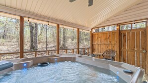 A hot tub with a wooden deck, a ceiling fan, and a view of the forest. - COZY COTTAGE - Private Hot Tub and Fire Pit (Branson)