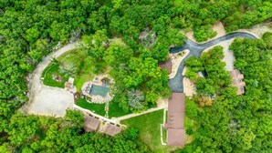 An aerial view of a residential area with a winding road, a swimming pool, and a well-maintained lawn. - COZY COTTAGE - Private Hot Tub and Fire Pit (Branson)