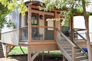 A wooden structure with a covered porch, a staircase, and a fenced area. - Brand new waterfront Cabin with many amenities: Pool, hot tub & kayaking. - SG11 (Seguin)