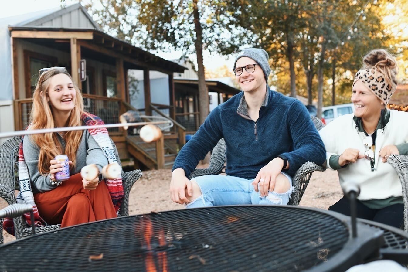 Un groupe de personnes est assis autour d’un barbecue dans un cadre extérieur, avec une structure en bois en arrière-plan.