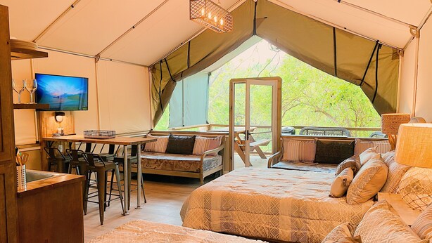 A tented accommodation with a dining area, a TV, and a bed with patterned bedding.