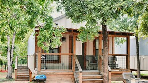 A wooden deck with a chair, a barbecue grill, and a covered seating area. - Wow! Brand new Creekfront Cabin! Hot tub, hiking, kayaking & more! - SG6  (Seguin)