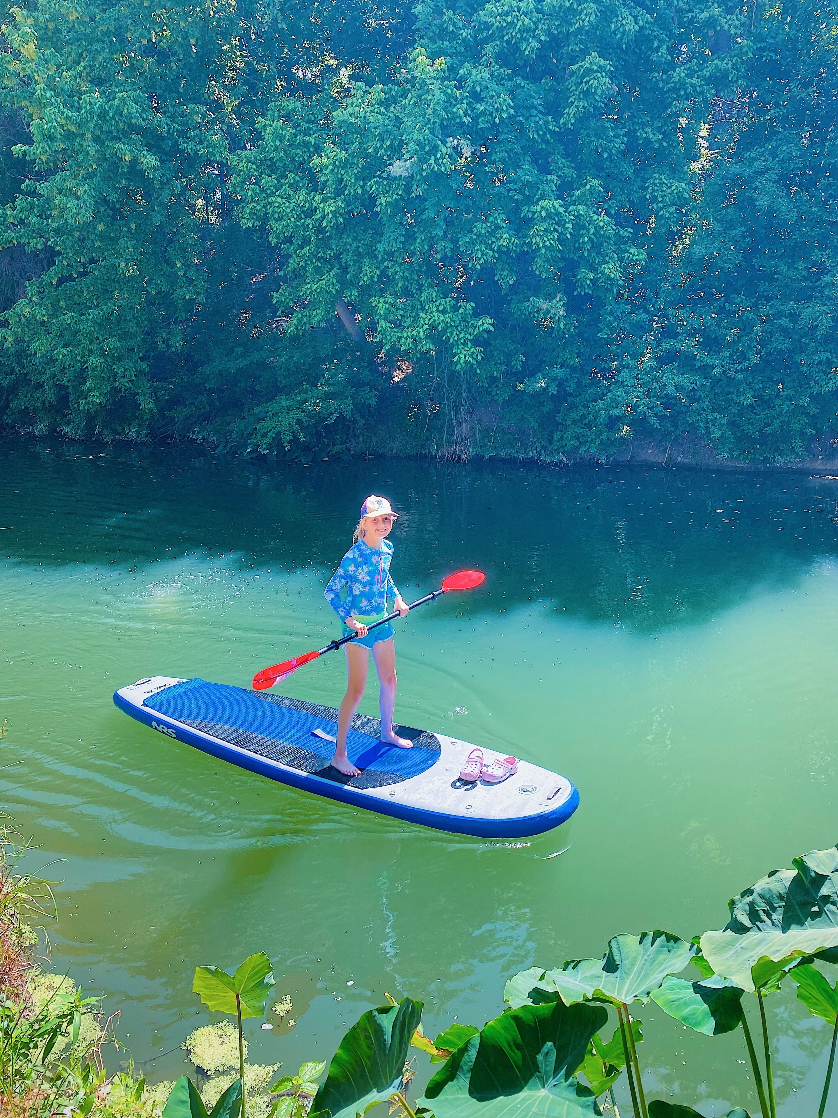 A person standing on a paddleboard in a body of water surrounded by dense greenery.