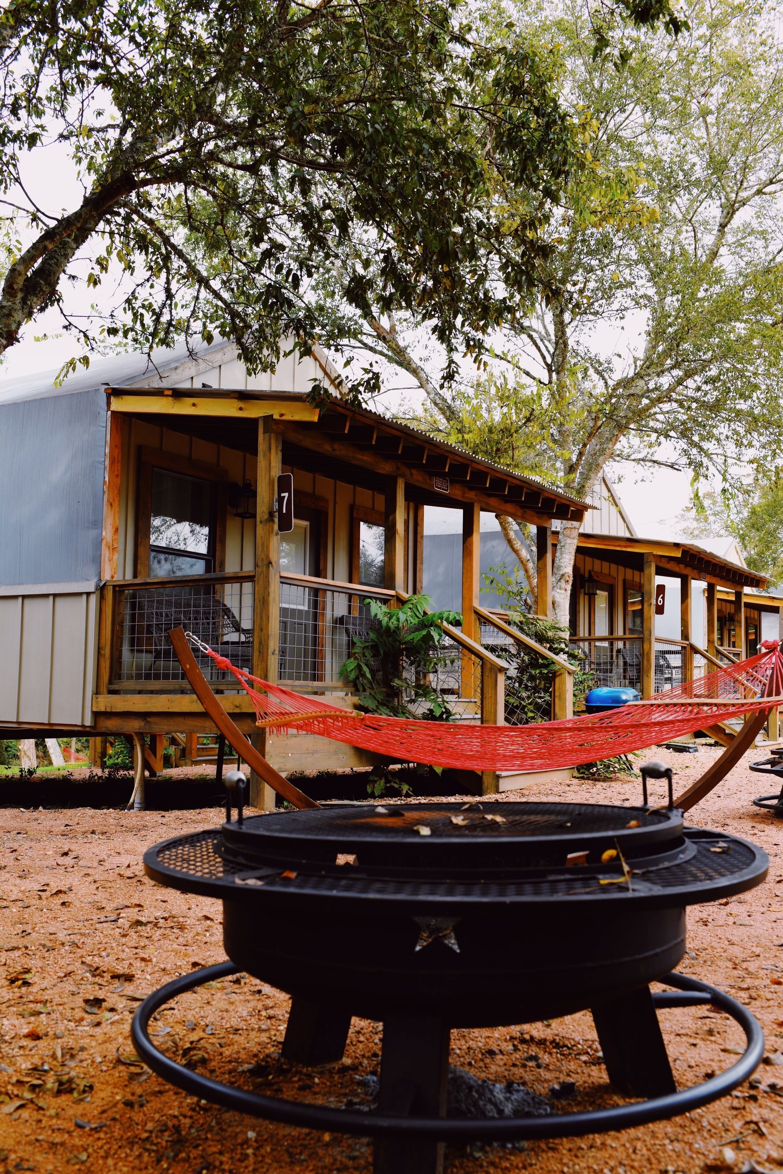 A rustic wooden cabin with a hammock and a circular fire pit.