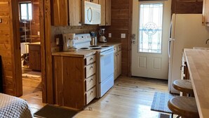 A wooden cabin interior with a kitchen area, including a stove, refrigerator, and cabinets. - Charming Cabin on the San Marcos River, comfortable, clean, fun, lots to do! L3 (Kingsbury)