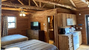A cabin interior with two beds, a television, a kitchenette, and a ceiling fan. - Charming Cabin on the San Marcos River, comfortable, clean, fun, lots to do! L3 (Kingsbury)