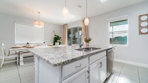 A modern kitchen with a granite countertop, white cabinetry, and a built-in dishwasher. - Lovely Pool Home With Spa Close to Area Attractions (Davenport)