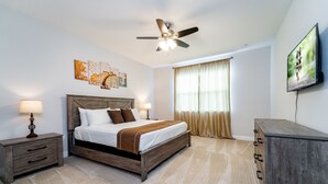 A bedroom with a wooden bed, nightstands, a ceiling fan, a large window with curtains, and a TV on the wall. - Lovely Pool Home With Spa Close to Area Attractions (Davenport)