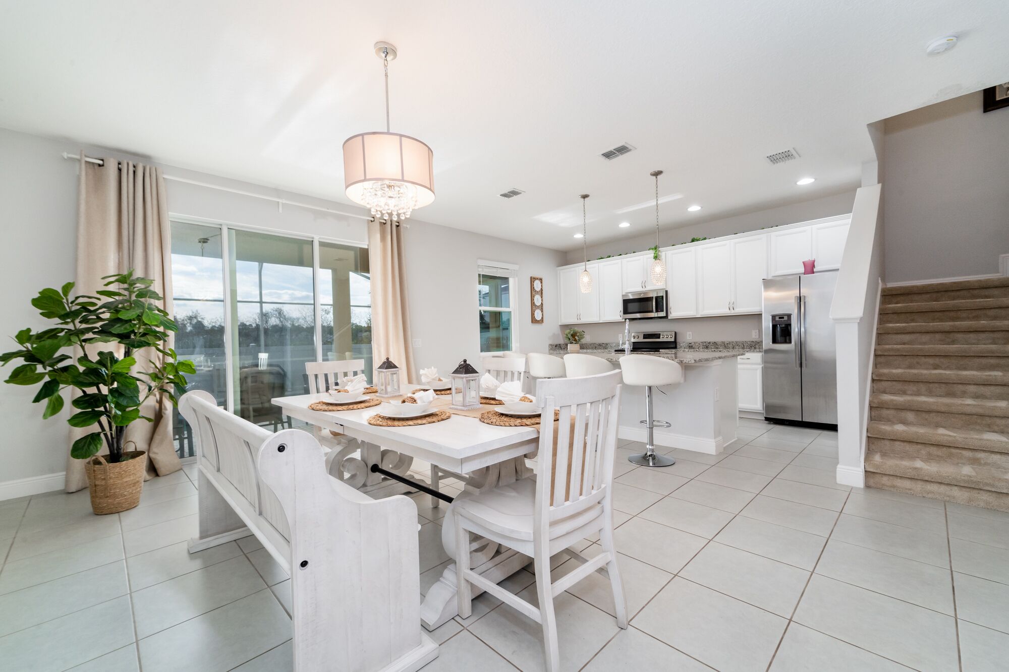A modern kitchen with white cabinets, stainless steel appliances, and a dining area with white chairs and a table set for four.