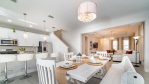 A modern kitchen with white cabinetry, a dining area with white chairs and a wooden table, and a living area with a sofa and a TV. - Lovely Pool Home With Spa Close to Area Attractions (Davenport)