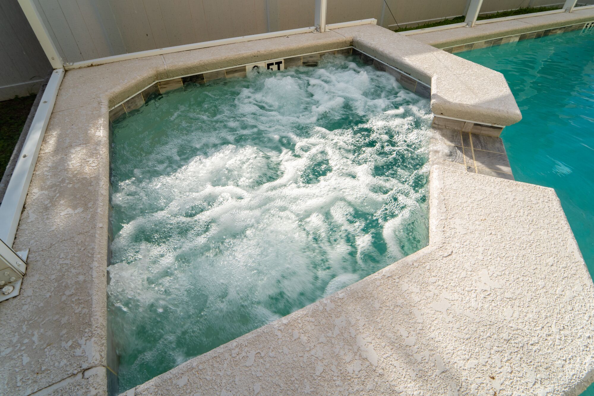 Un jacuzzi con borde de piedra y una piscina al fondo.
