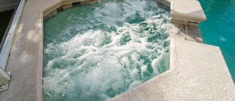 Un jacuzzi con borde de piedra y una piscina al fondo.