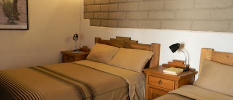 A hotel room with two beds, wooden headboards, a brick accent wall, bedside lamps, and a framed picture on the wall.