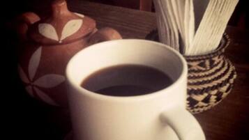 A white cup of coffee on a saucer, a patterned teapot, and a woven napkin holder.