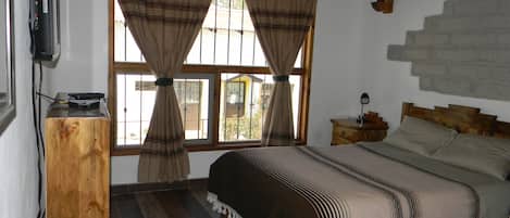 Un dormitorio con cama, mesita de noche, lámpara y ventana con cortinas.