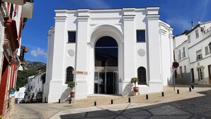 A white building with an arched entrance, a sign indicating a direction, and potted plants at the entrance. - Ubrique Rural Loft (Ubrique)