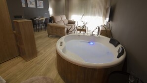 A modern hotel room with a large bathtub, a dining area with a table and chairs, and a sofa. - Ubrique Rural Loft (Ubrique)