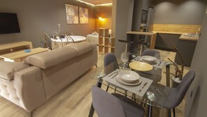 A modern living room with a sofa, dining table set for four, and a kitchen area with appliances. - Ubrique Rural Loft (Ubrique)