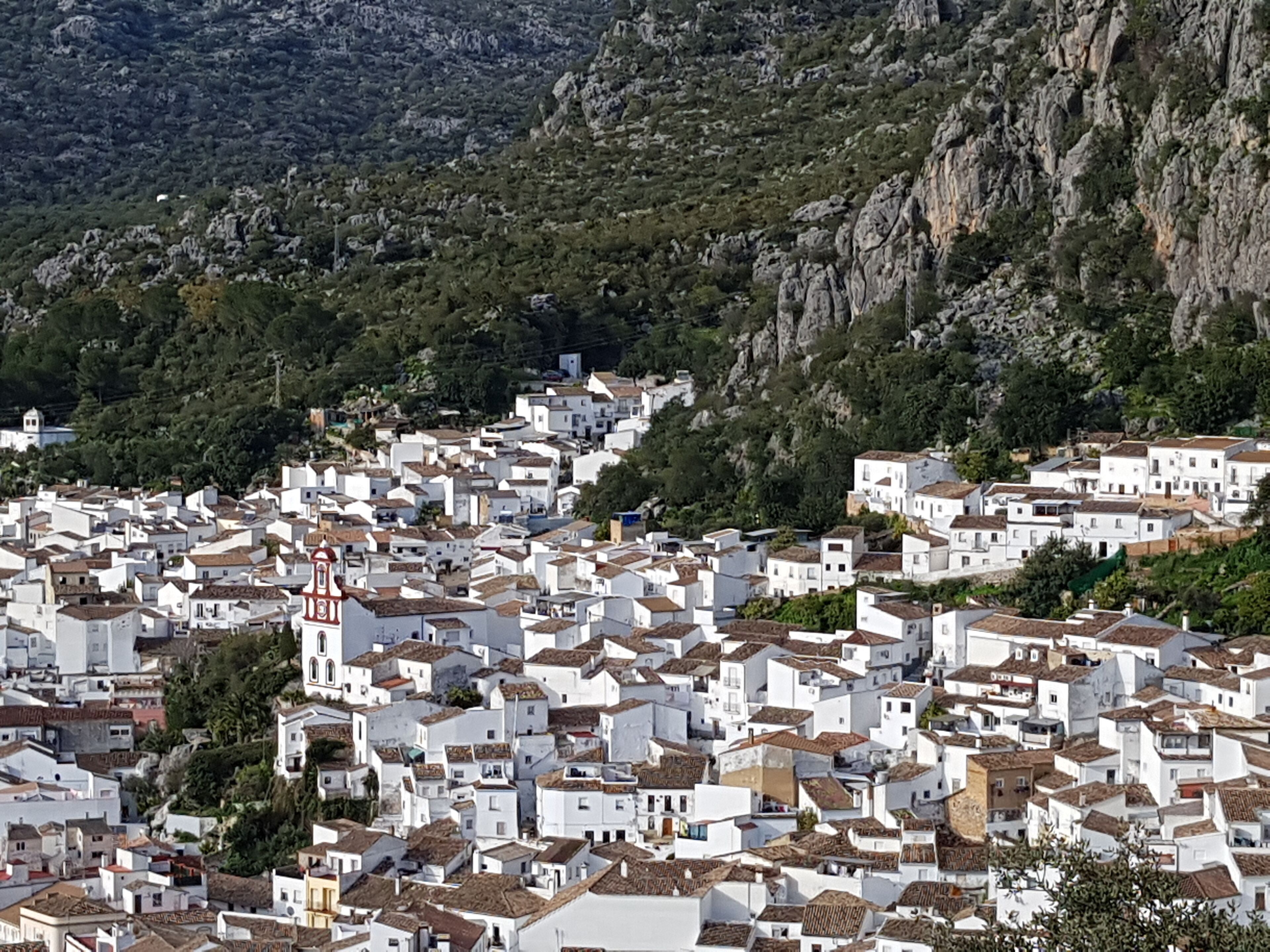 Un pueblo costero denso y abarrotado, con edificios blancos y tejados de tejas rojas, rodeado de acantilados escarpados y vegetación.