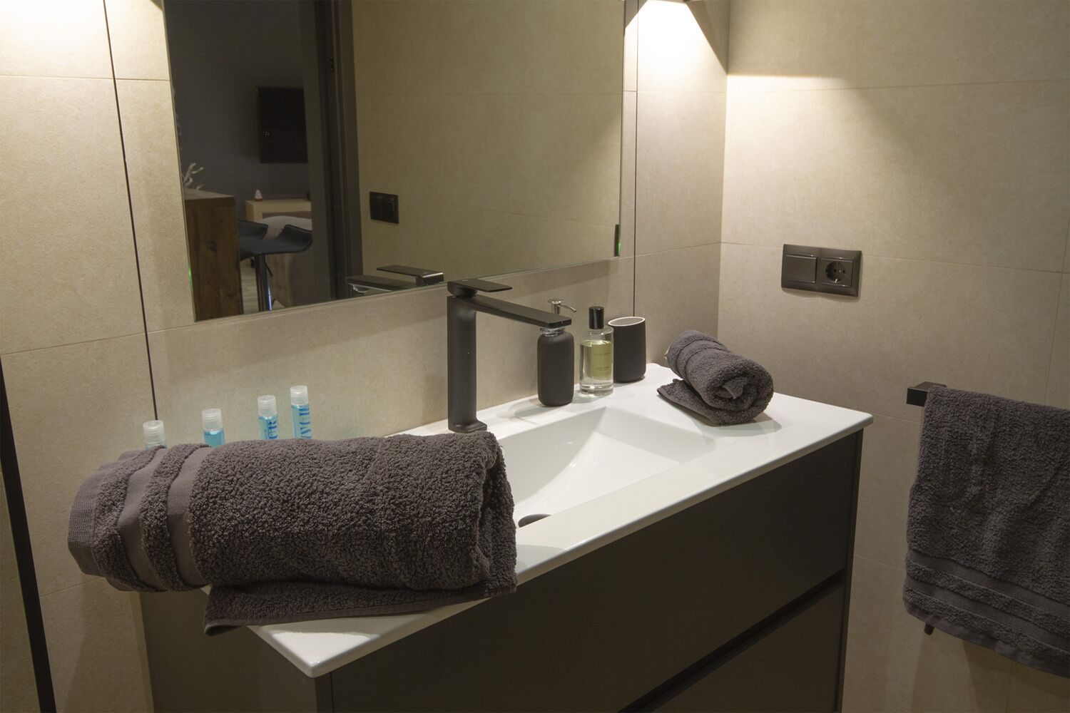 Un baño moderno con un lavamanos blanco, toallas oscuras y artículos de aseo.